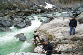 Rocky boulder shore along the base of the glacier river at keyhole hot springs, british colombia. Friends depicted walking along the shire line,