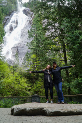 Alicja and her friend with arms wide open enjoying the mist coming of off the falls, standing on a stone platform