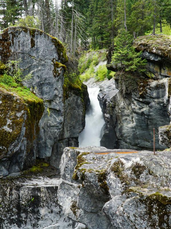 A glimpse of Nairn falls between a crevis in the rocks from a lookout point. Large cliff rocks surround this beautiful multi-tier waterfall.