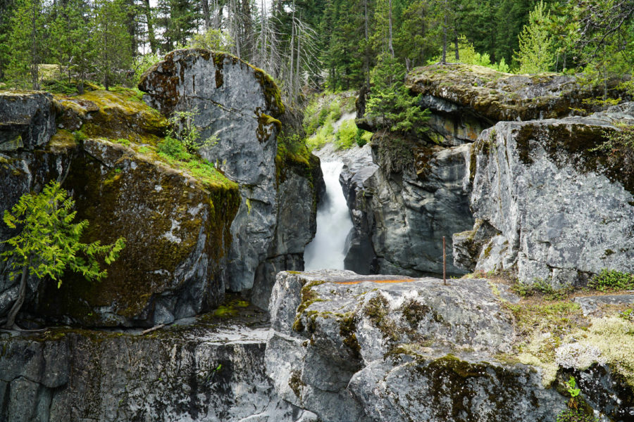 A glimpse of Nairn falls between a crevis in the rocks from a lookout point. Large cliff rocks surround this beautiful multi-tier waterfall.